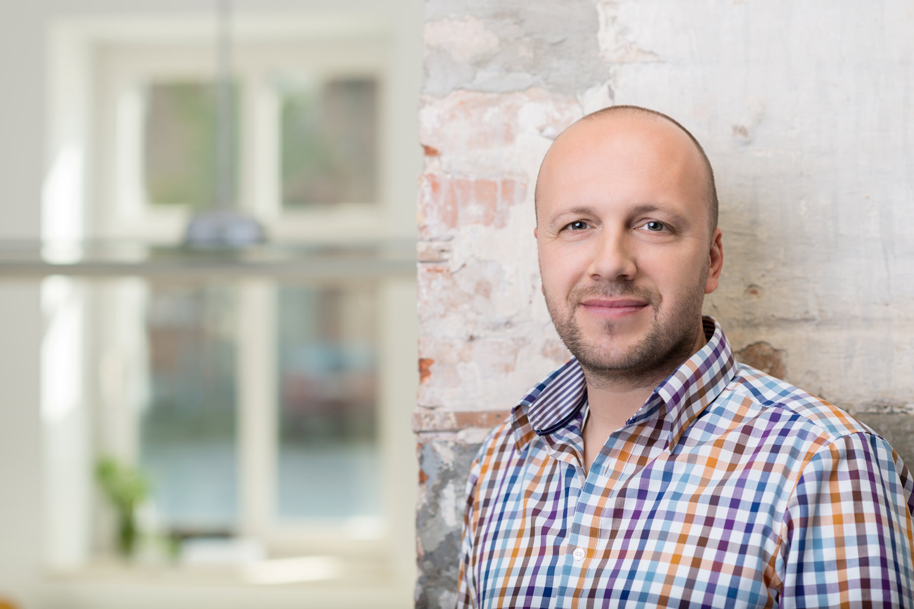 man smiling against an exposed brick wall