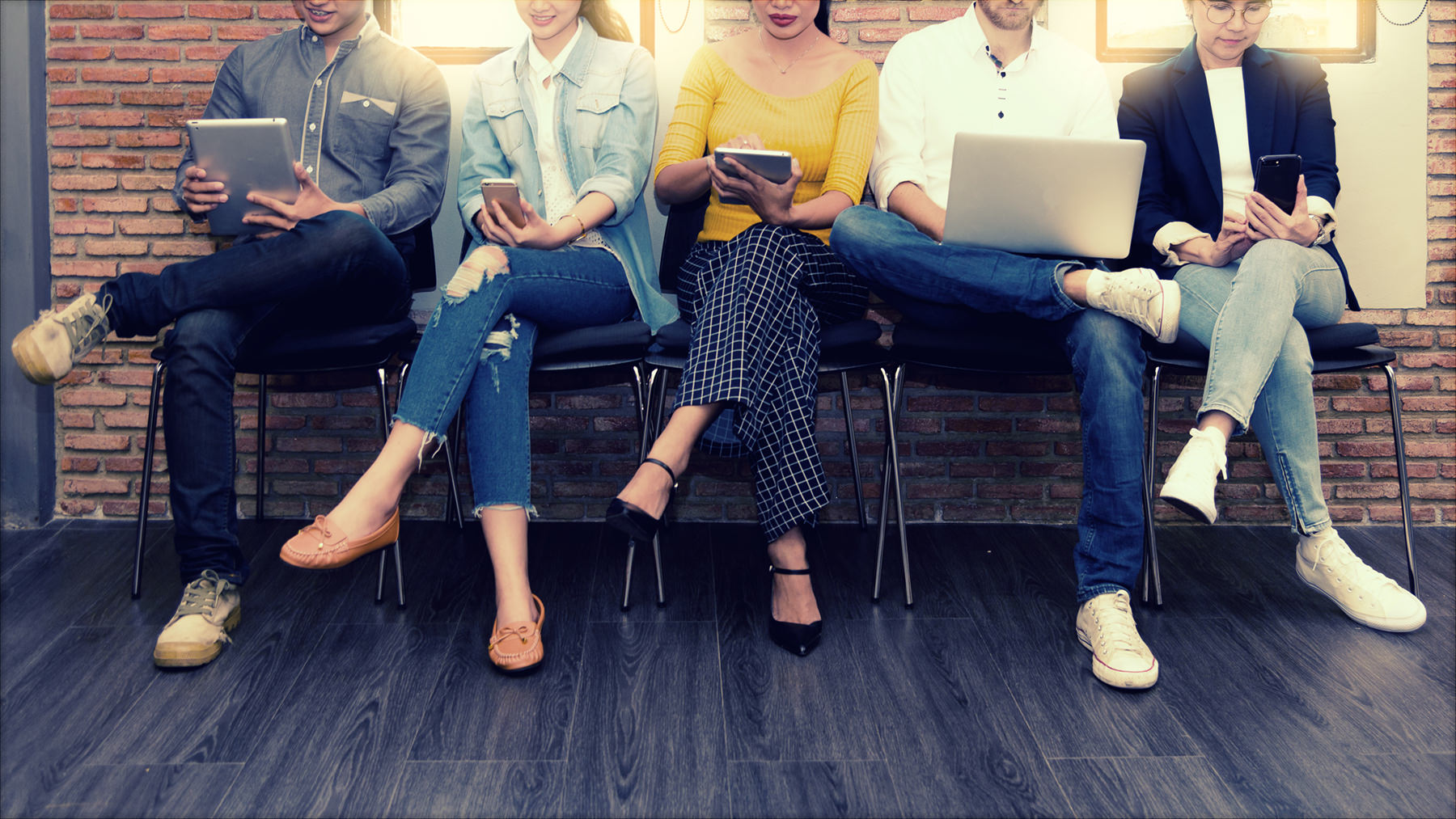 people sitting against a wall looking at mobile devices